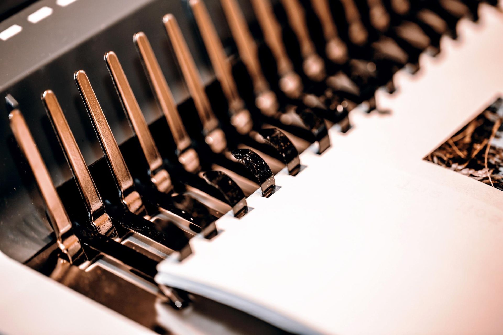 A close-up of a book binding machine with copper-colored prongs holding pages.