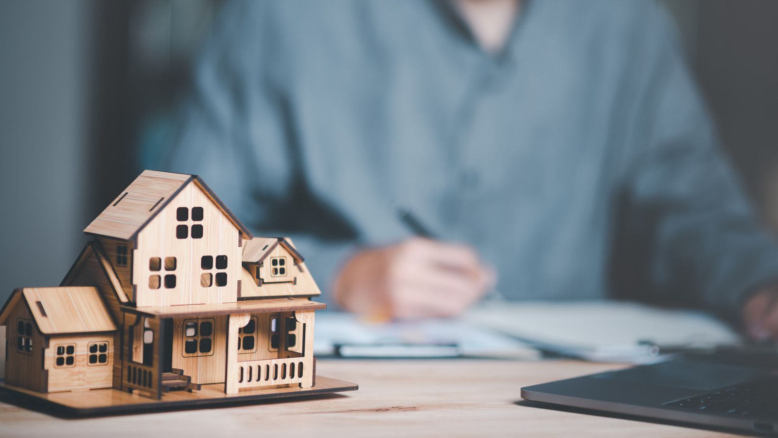 A model house is sitting on a table next to a person writing on a clipboard.