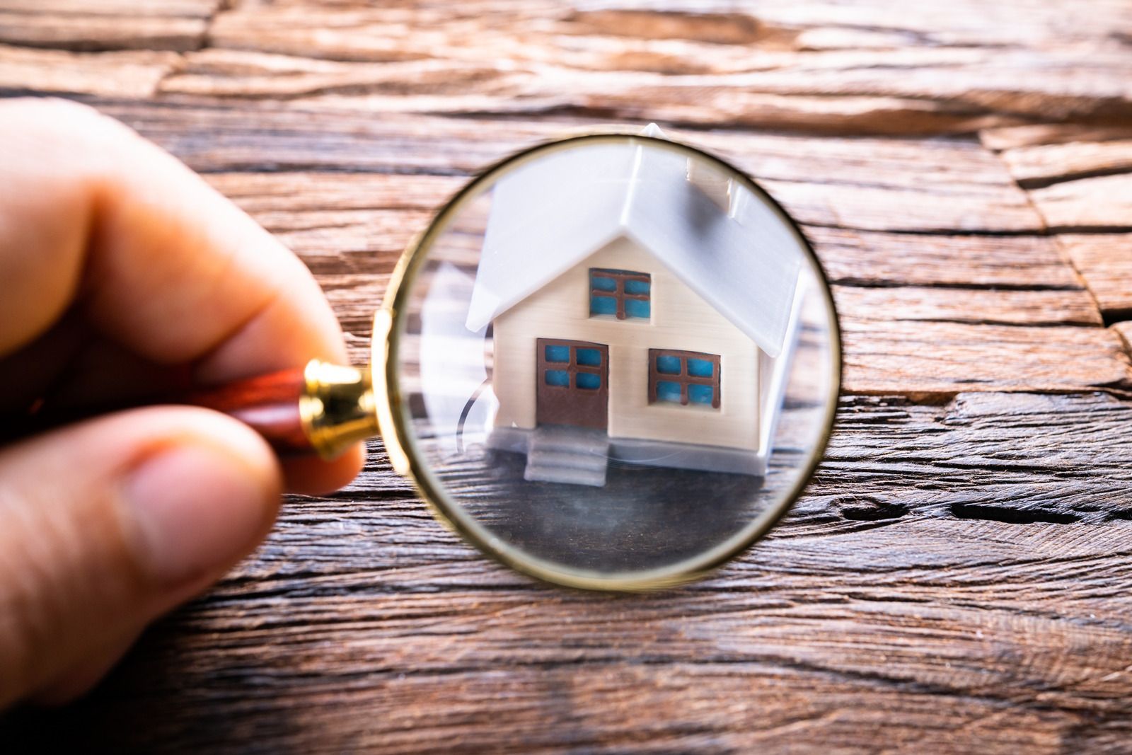 A person is holding a magnifying glass over a model house.