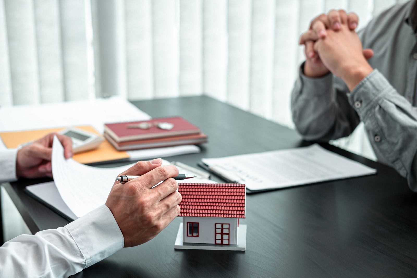 Real estate agent pointing to paperwork; discussing a deal with a client, house model on the desk.