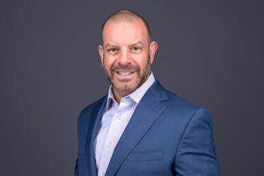 Smiling man in a blue suit jacket and light shirt against a gray background