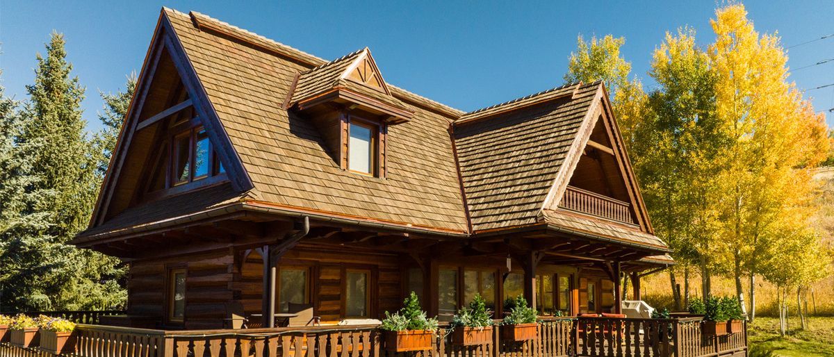 Wooden shingle roof of a house with a balcony and a view of trees and sky.