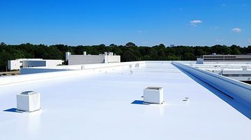 White commercial roof with two square units, blue sky, trees in the background.
