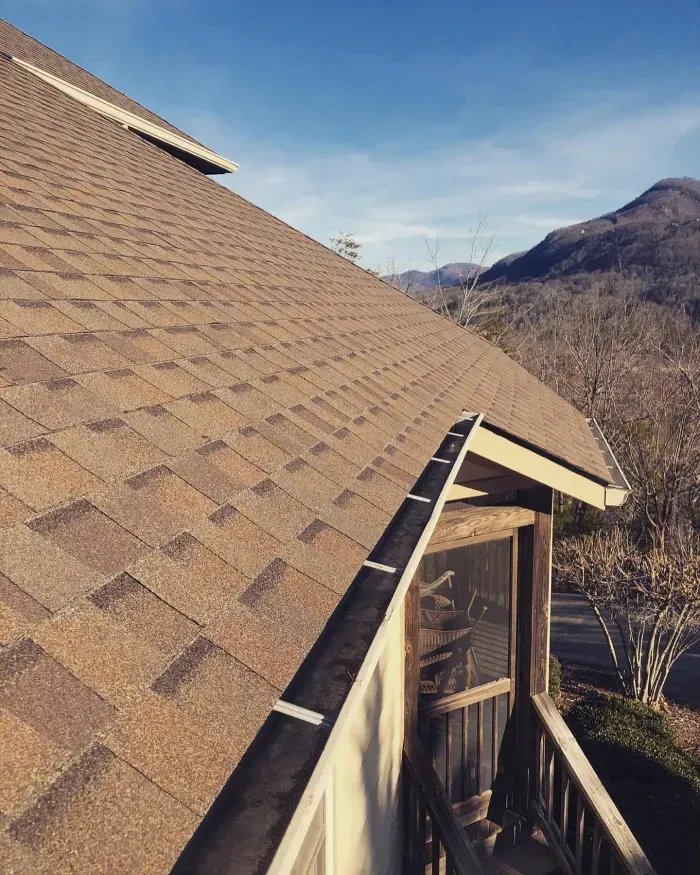 Brown shingled roof with a screened porch overlooking mountains against a blue sky.