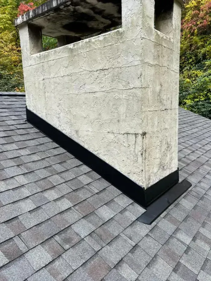 Chimney on a shingled roof with black flashing.