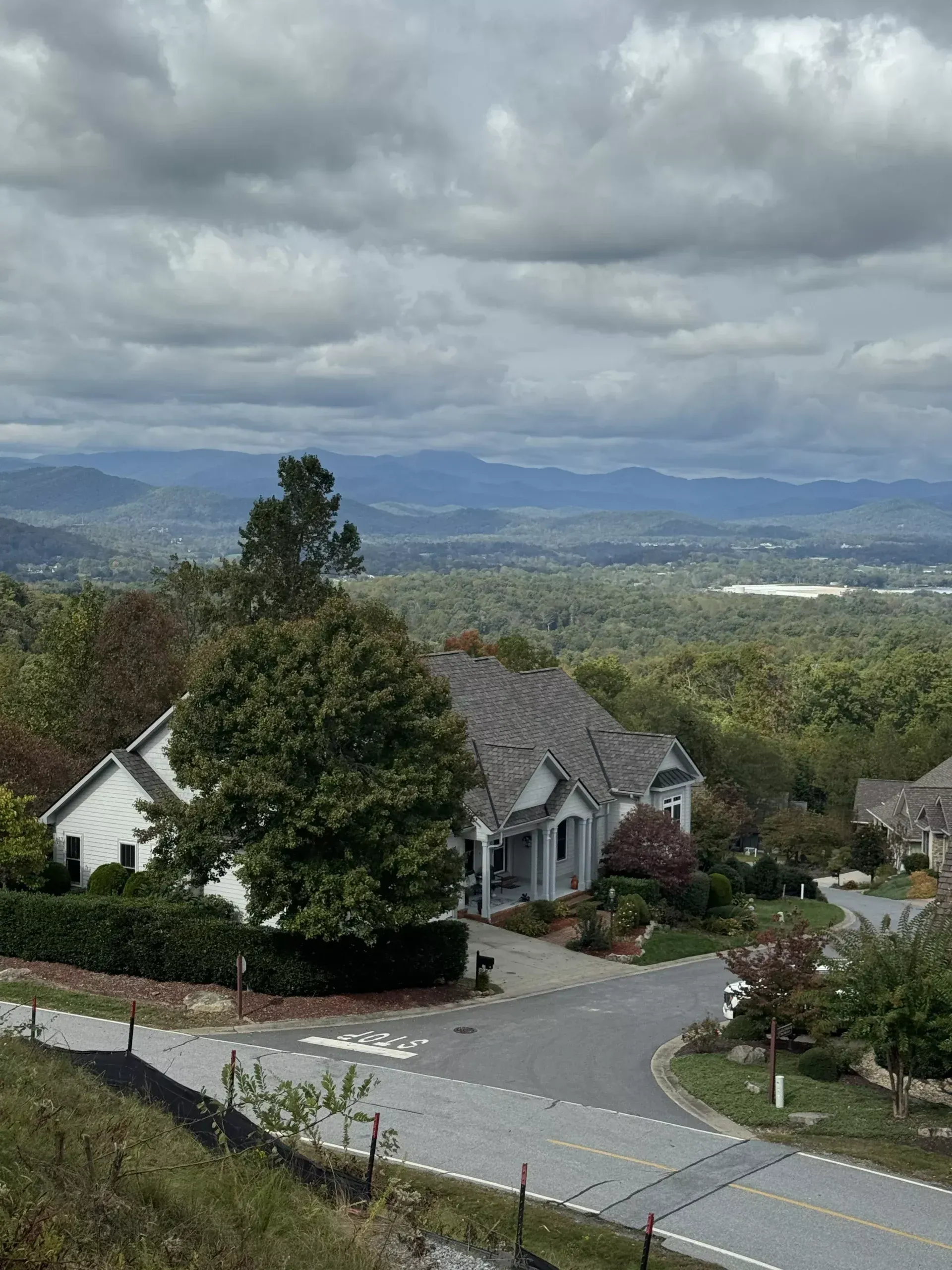 House on a hillside with a view of rolling green hills, mountains, and a cloudy sky.