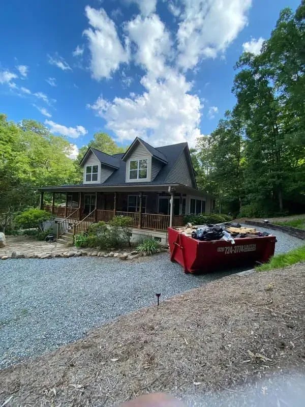 House with gray siding and porch, red dumpster in driveway. Blue sky, trees.