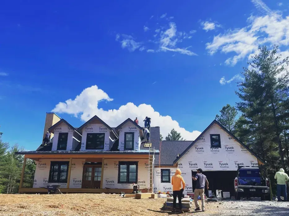 House under construction with workers, blue sky with clouds.