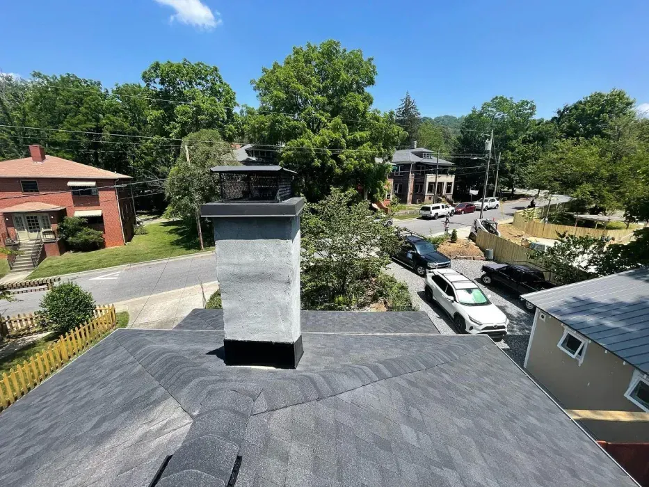 Gray roof with a chimney and a view of a street, houses, and trees on a sunny day.