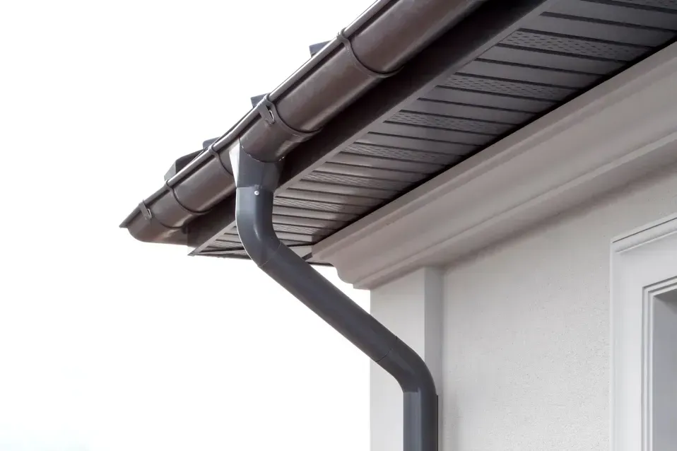 Brown roof gutters and downspout on a house with white siding and a brown soffit.