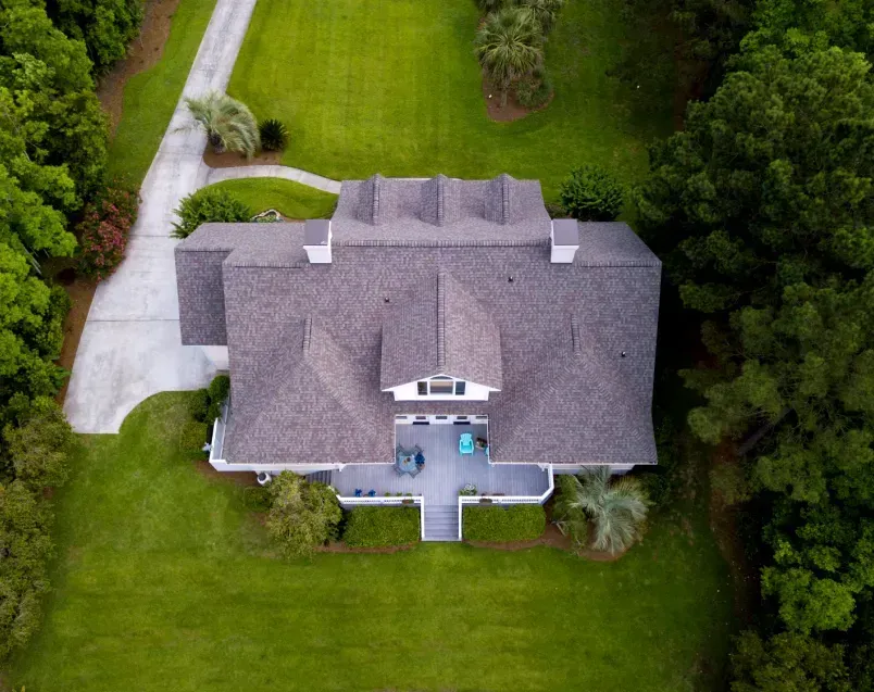 Aerial view of a house with a gray roof and white siding, surrounded by green grass and trees.