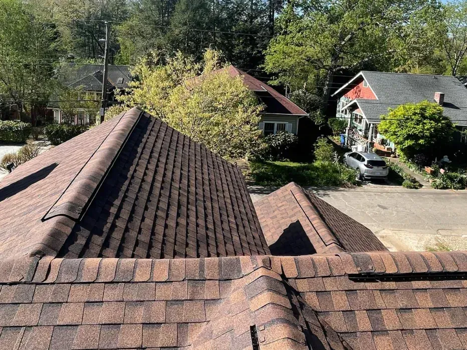 Brown asphalt shingle roof on a house, with a view of nearby houses and trees on a sunny day.