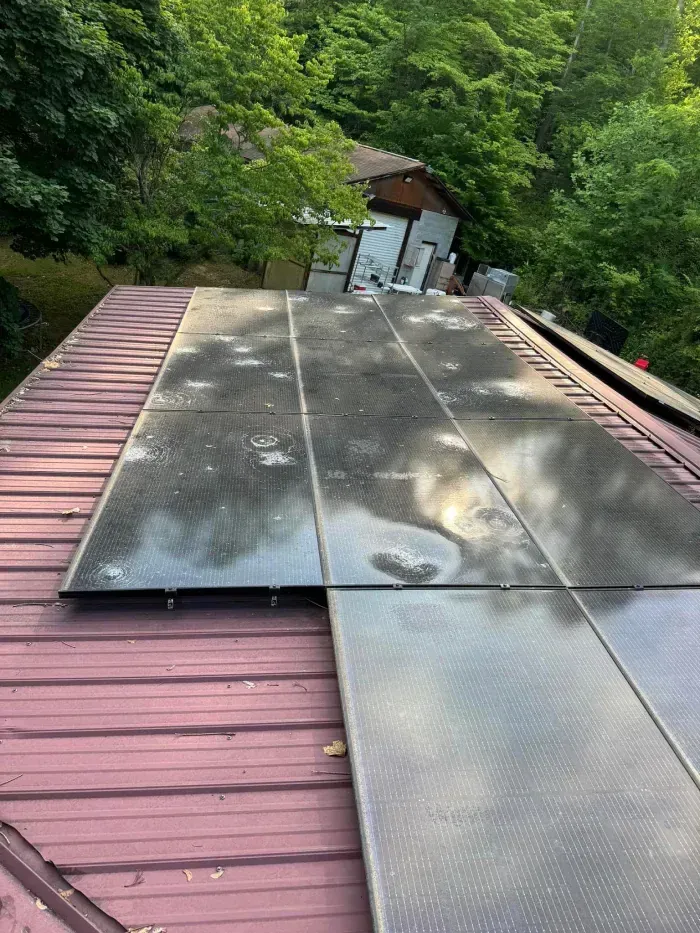 Solar panels on a red metal roof, surrounded by trees.