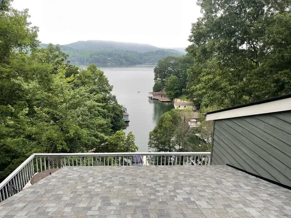 View from a deck overlooking a lake with trees and houses. Gray shingles and metal railing in foreground.