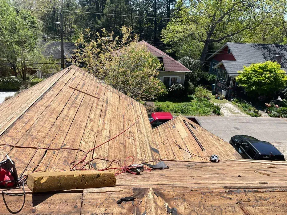 Rooftop with exposed wooden sheathing, tools, and a partial view of neighborhood houses.