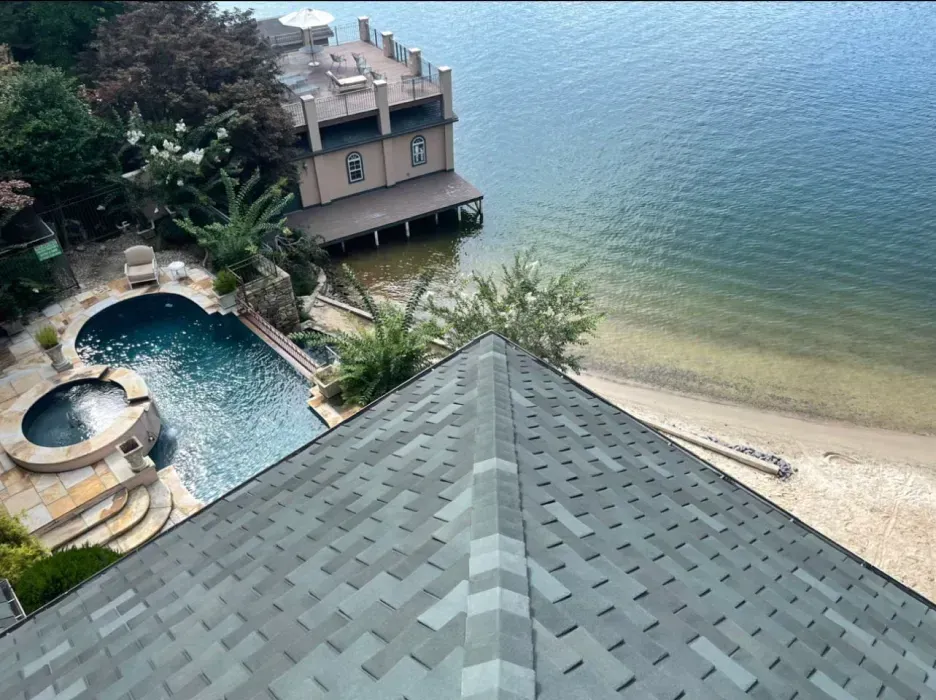 Overhead view of a house with a dark gray roof, swimming pool, and lakefront property.