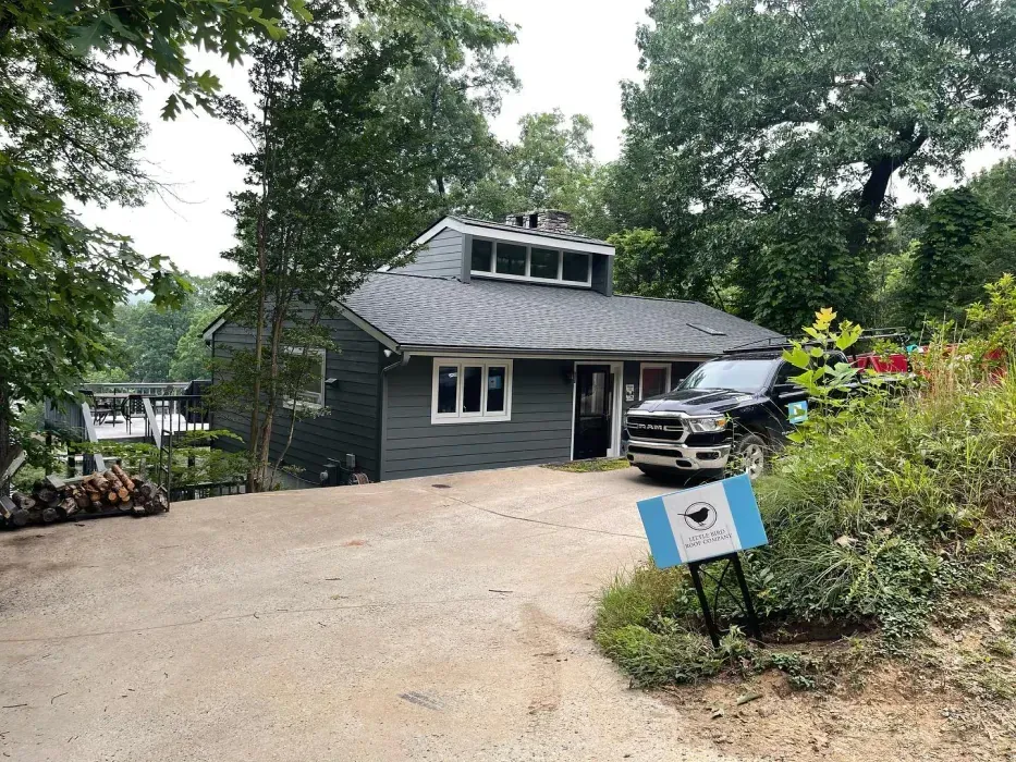 Dark gray building with white trim, a black truck, and a sign in front, surrounded by trees.