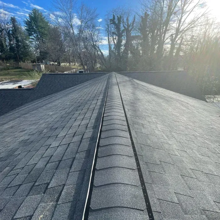 Dark asphalt shingle roof on a house, angled view of the ridge, clear blue sky.