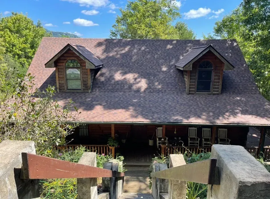 Rustic cabin with dormer windows, porch with rocking chairs, and stone stairs leading up.