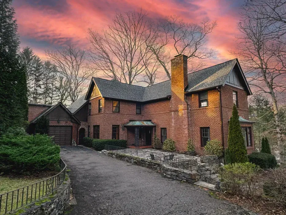 Brick house with a long driveway under a colorful sunset.