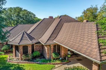 Red metal roof with a skylight and a chimney against a backdrop of green trees.