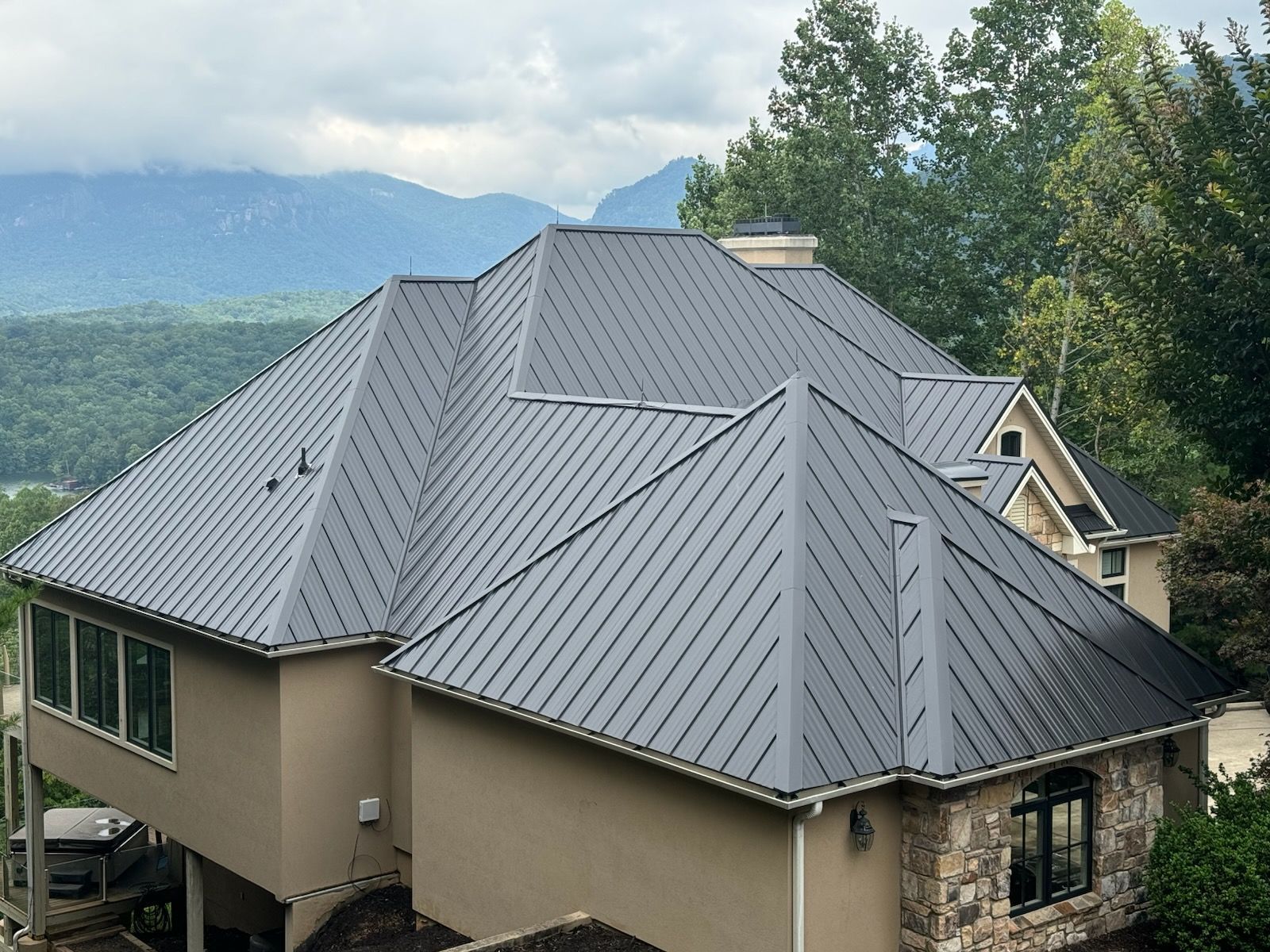 Gray shingled roof of a house, seen from above with a driveway and trees in the background.