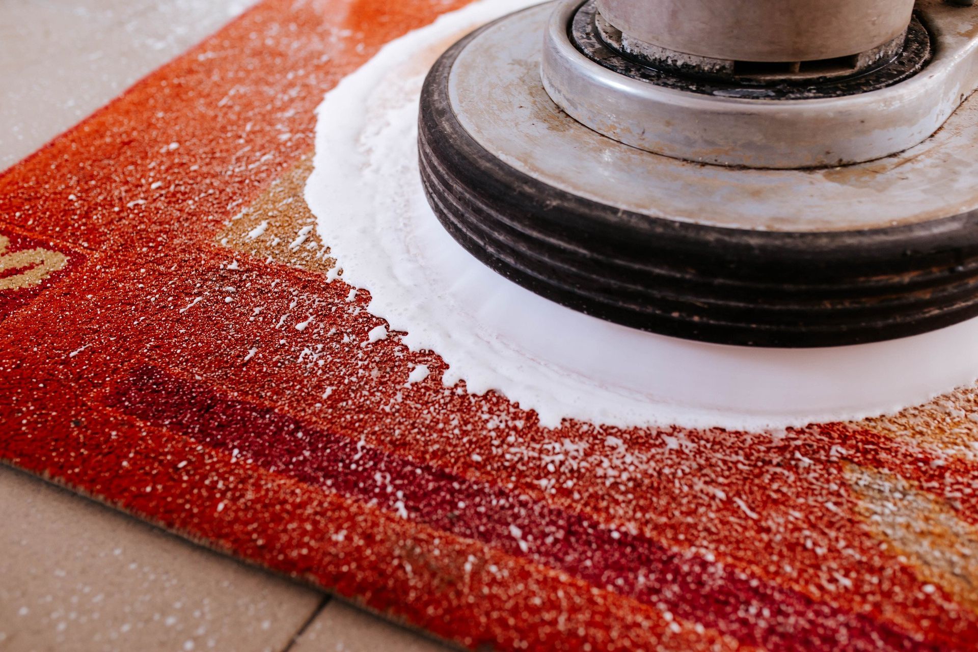 A red rug is being cleaned with a machine.