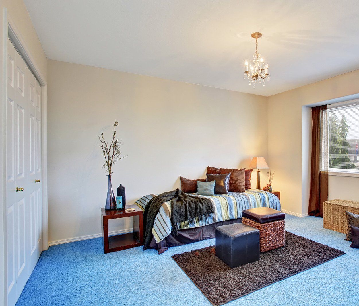 A bedroom with a bed , ottoman , rug and chandelier.