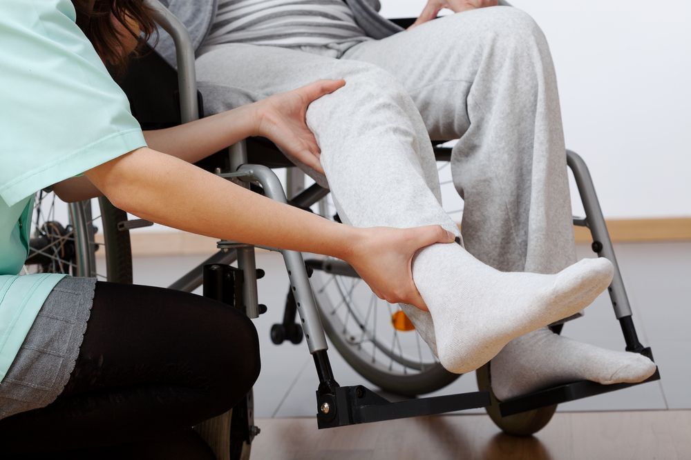 A woman is helping a man in a wheelchair with his leg.