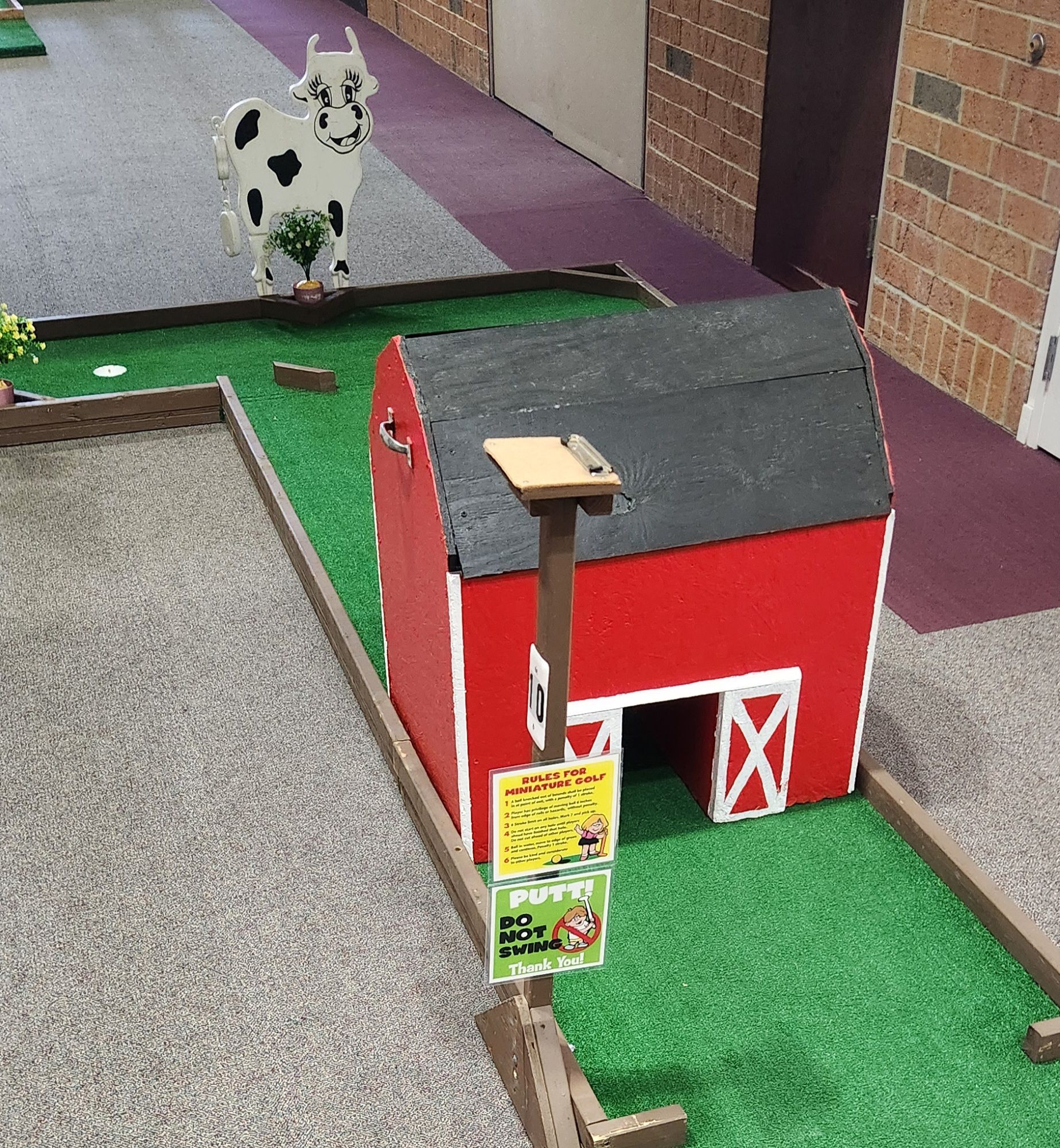 Miniature golf course with a red barn and a cow cutout.
