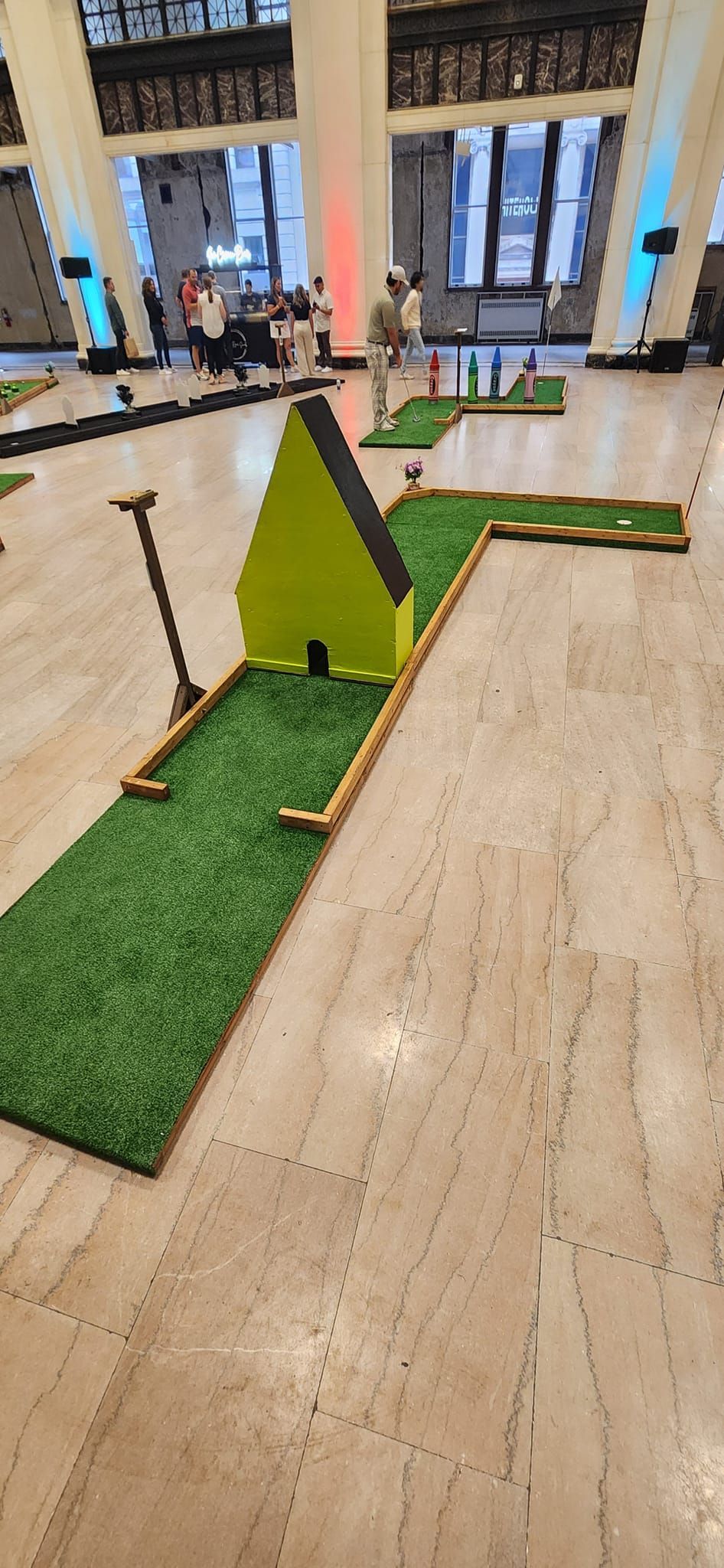 Mini golf course set up indoors, featuring a green hut obstacle.