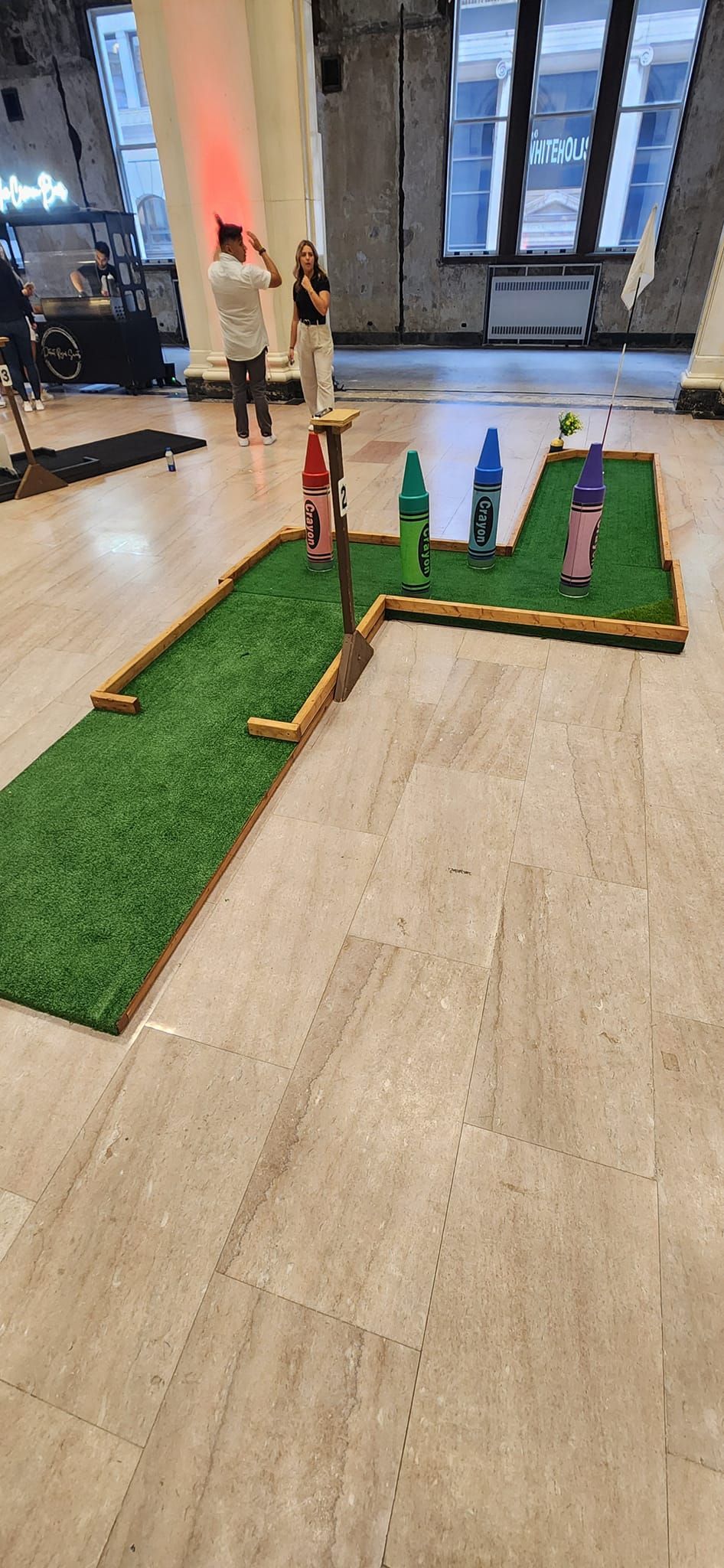 Mini golf course set up indoors with people nearby.
