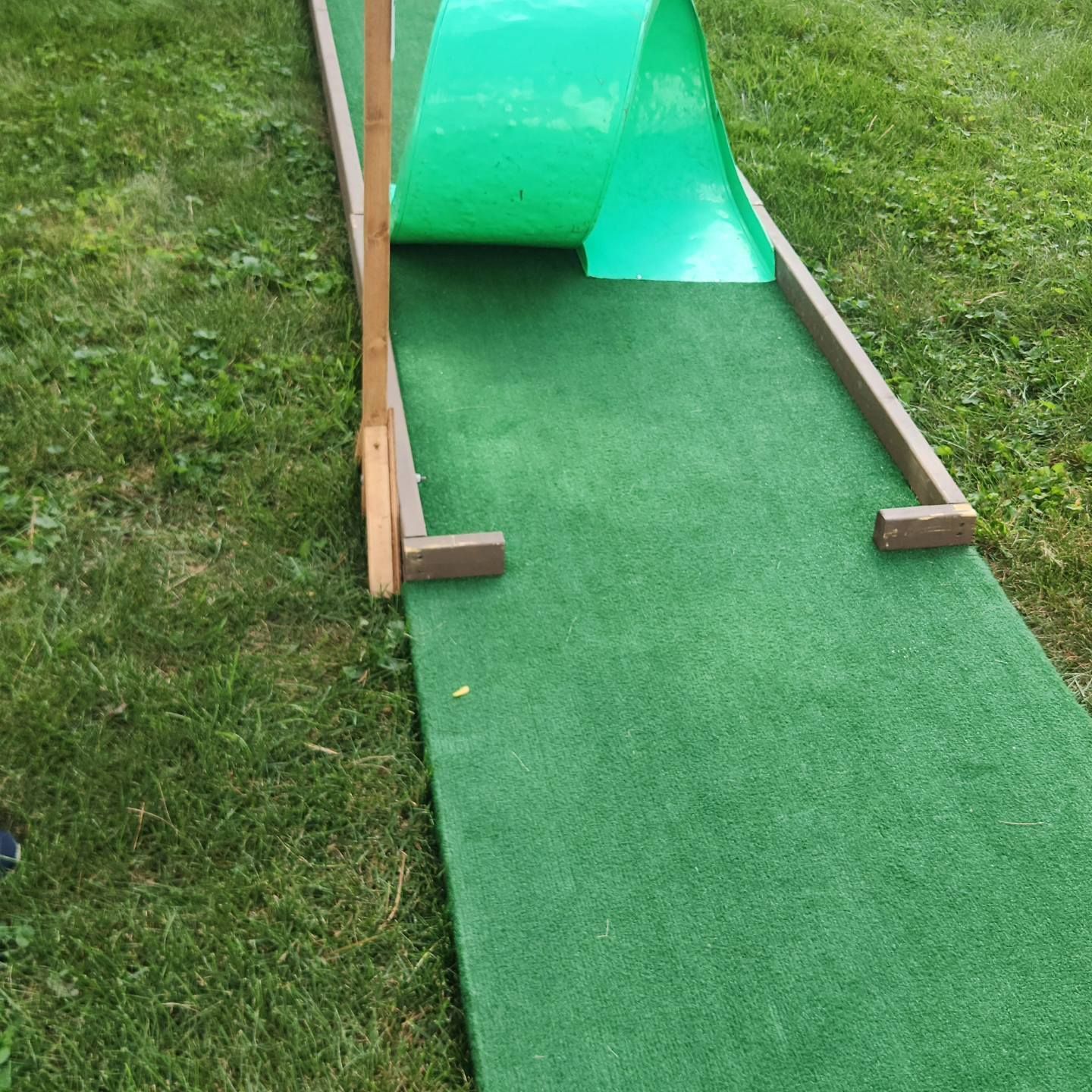 Mini golf course hole with green turf, wooden frame, and arched ramp.