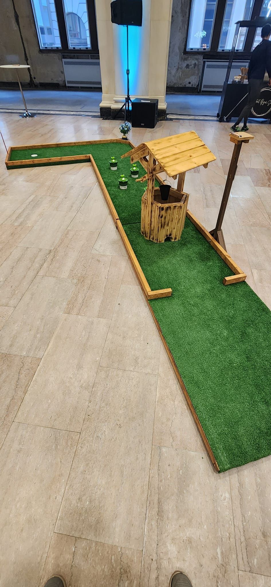 Miniature golf course with a well and green turf on a tan floor.
