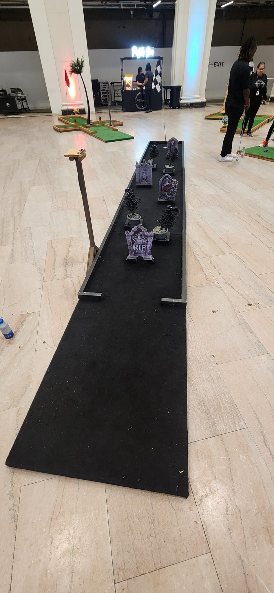 Indoor mini golf setup with figurines on a long black mat. A person stands nearby.