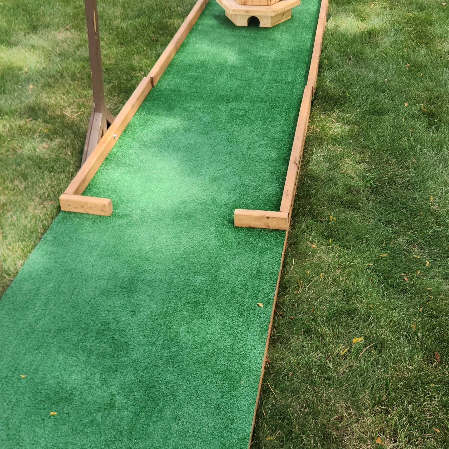 Miniature golf course with green turf and wooden borders on grass.