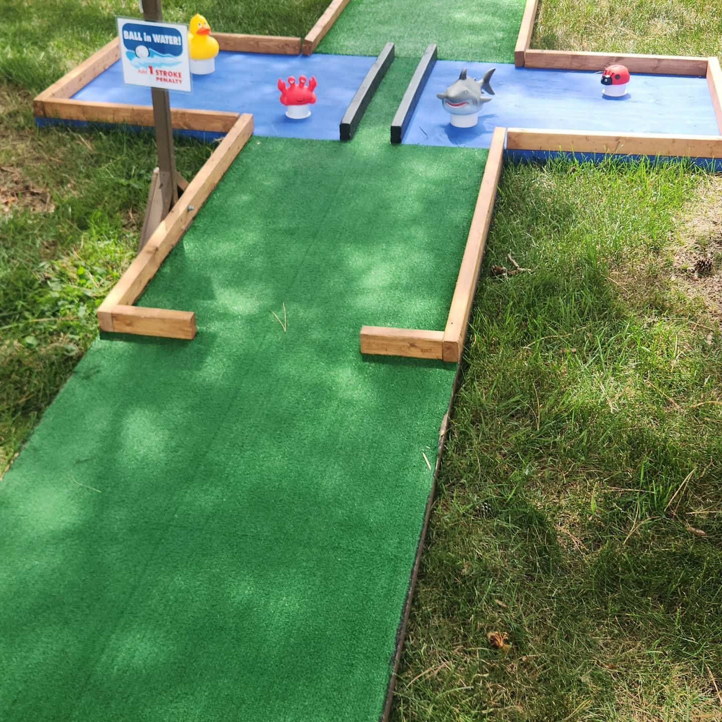 Miniature golf course with green turf, blue water features, and wooden borders.