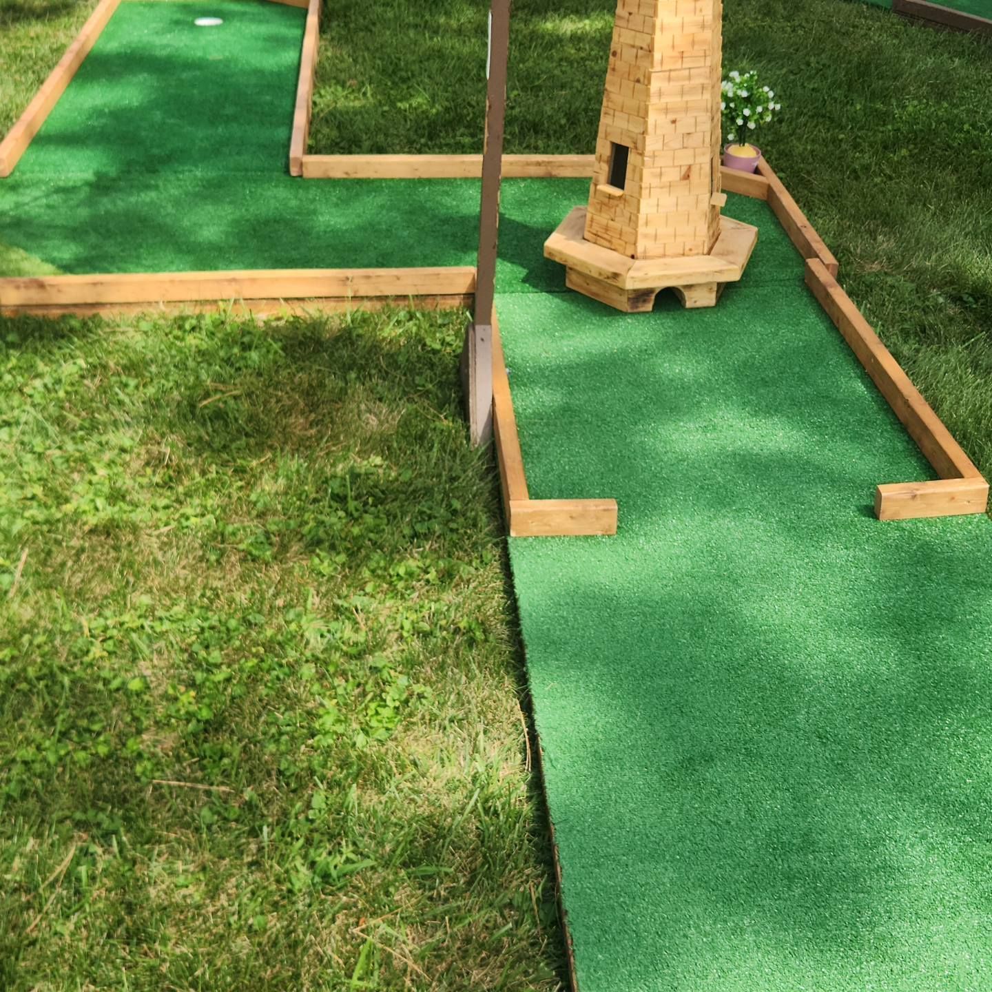 Miniature golf course with green turf, wooden borders, and a small lighthouse obstacle.