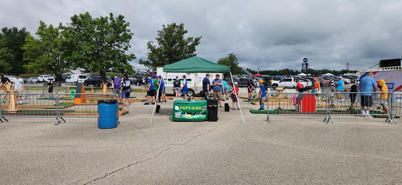 People at an outdoor event with tents, barriers, and vehicles under a cloudy sky.
