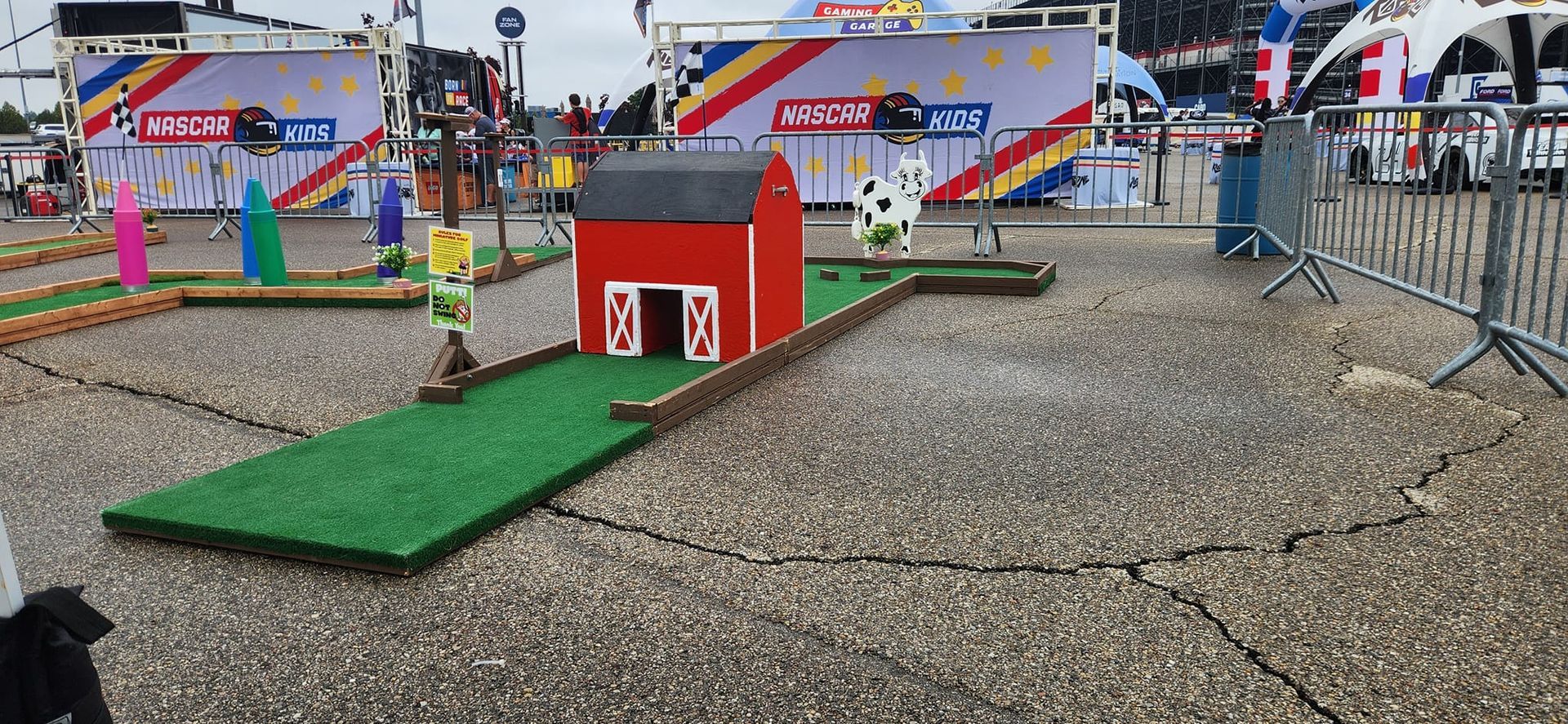 Miniature golf course with red barn obstacle. Green turf on a cracked asphalt surface.