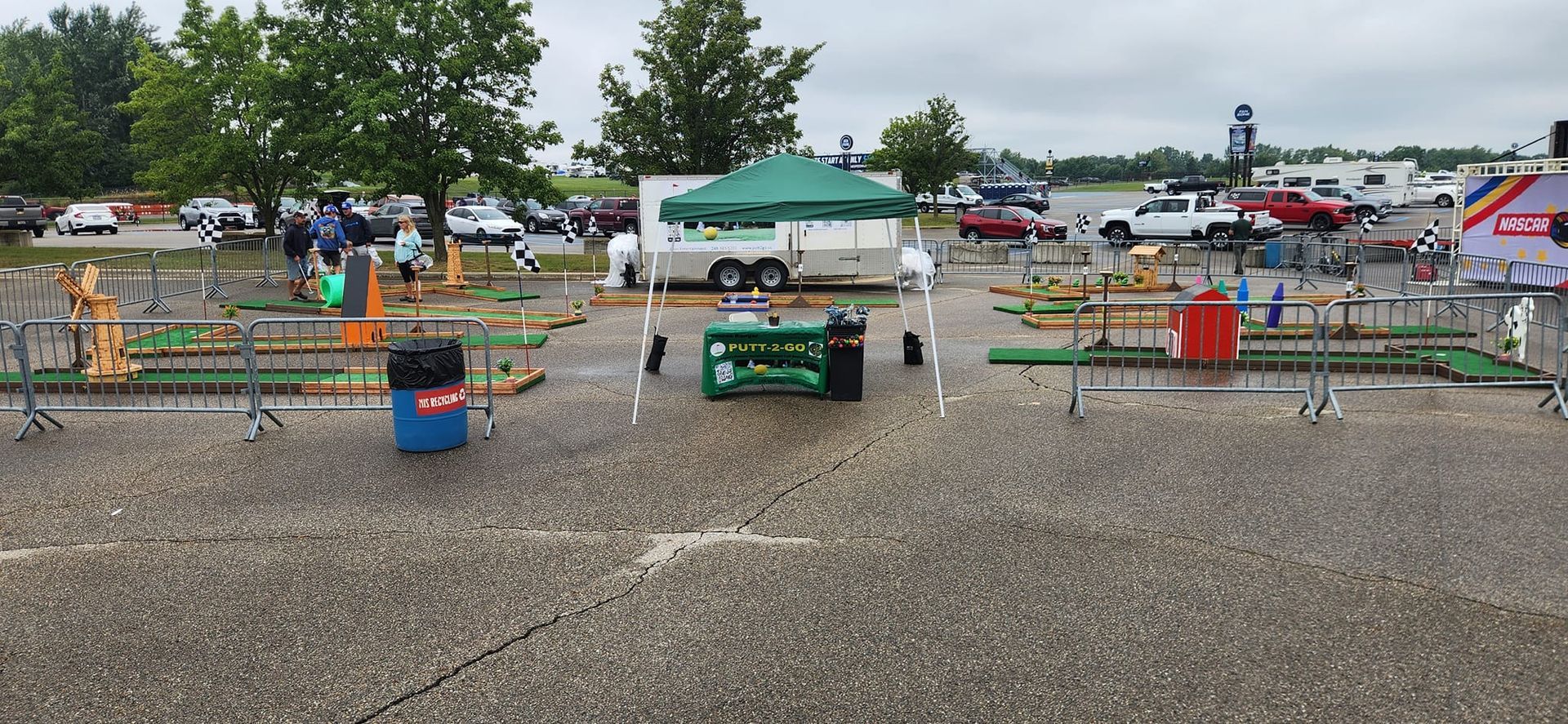 Miniature golf course set up in an outdoor parking lot with a green tent and tables.