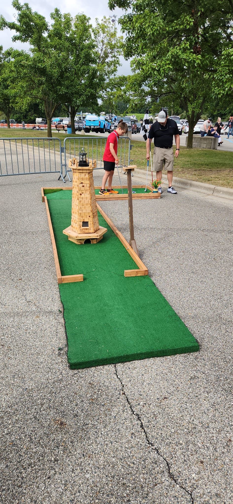 People playing miniature golf outside; a course with a tower and green turf.
