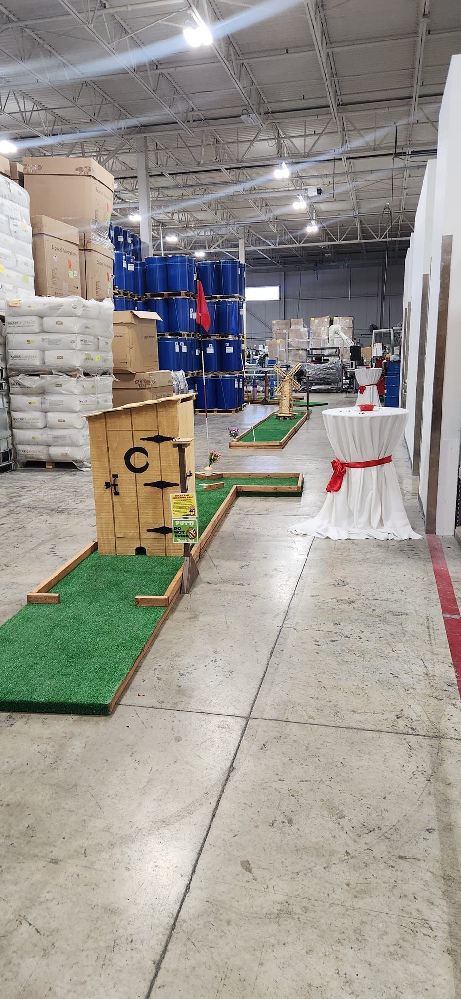Indoor mini-golf course set up in warehouse with wooden obstacles and green turf.