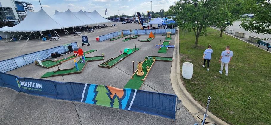 Miniature golf course with players and tents in an outdoor event setting.