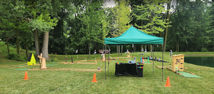 Mini golf course set up in a warehouse. Green turf, yellow obstacle, barrels on the left.