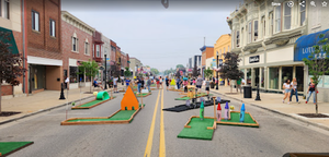 Miniature golf course set up in a parking lot. People and vehicles are visible.
