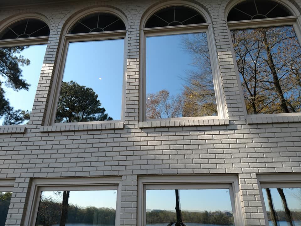 A white brick building with a lot of windows and trees reflected in the windows.