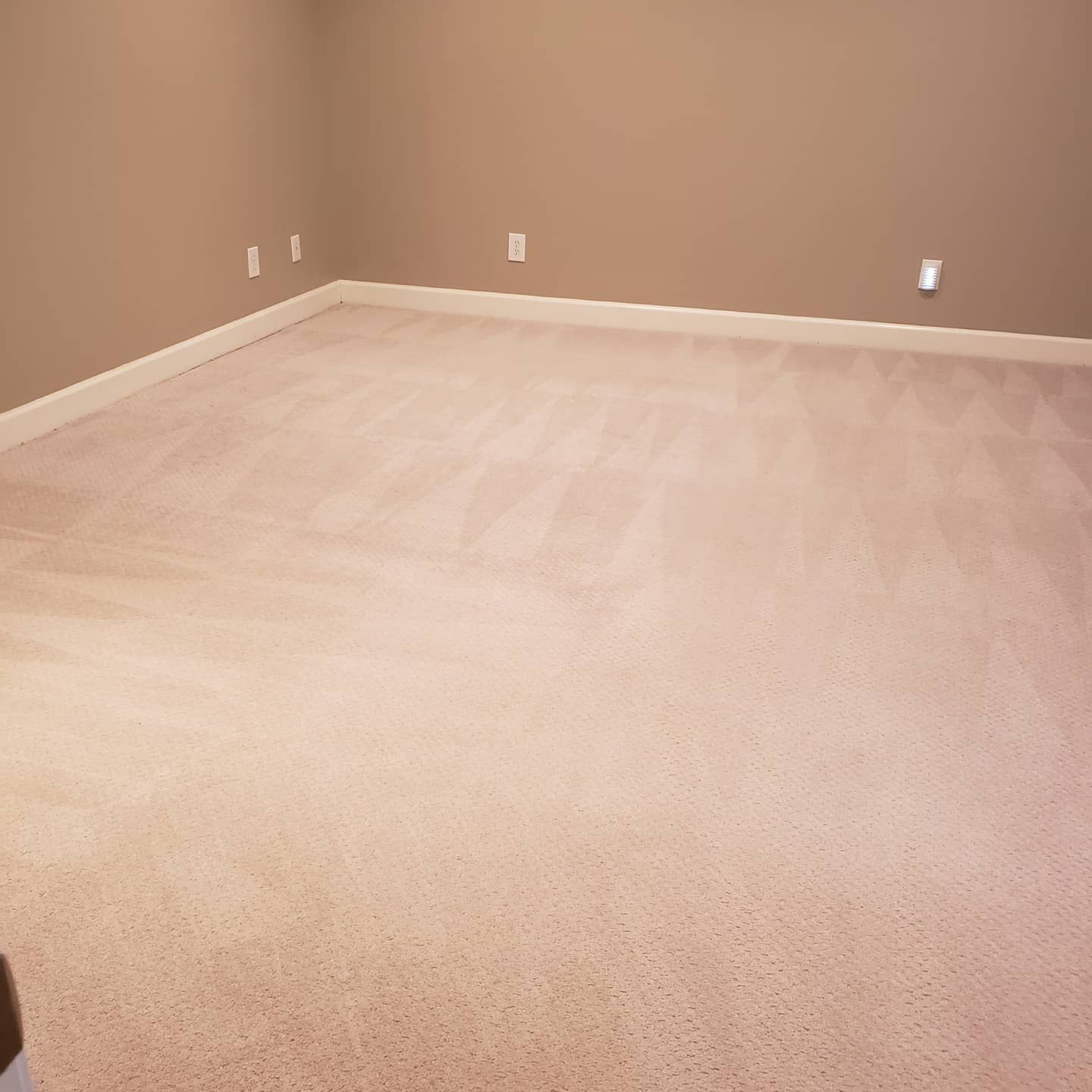 An empty room with a large carpeted floor and tan walls.