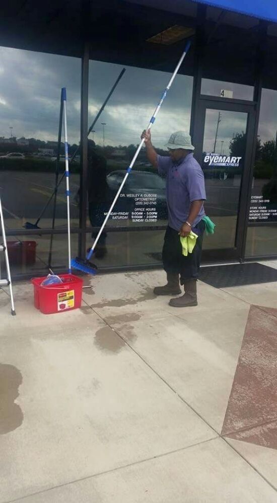 A man is cleaning the windows of a building with a mop.