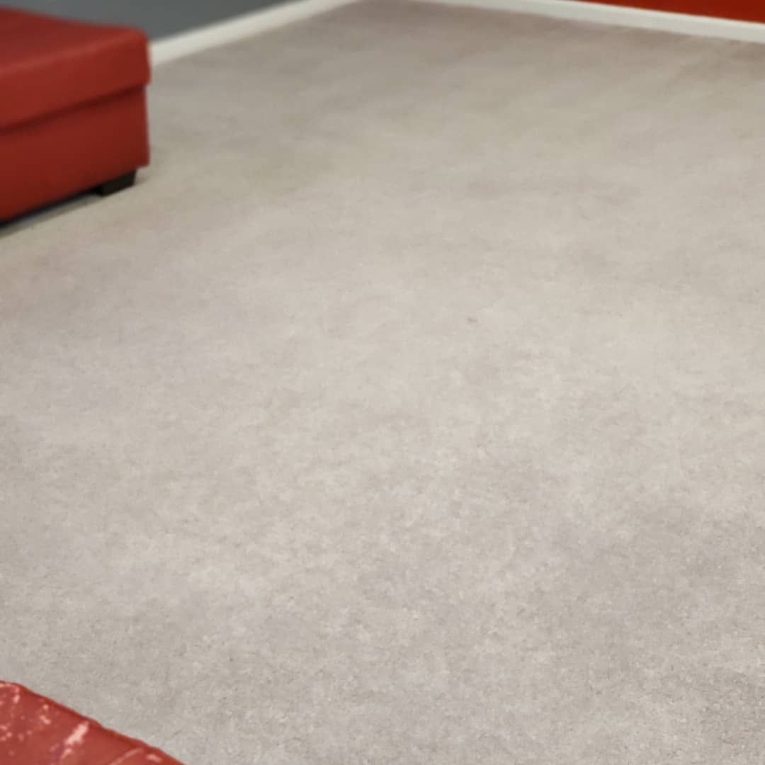 A living room with a gray carpet and a red ottoman.